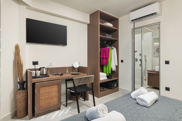 A modern hotel room with a bed, a desk with a chair, a wardrobe, a mirror, and a TV on the wall.