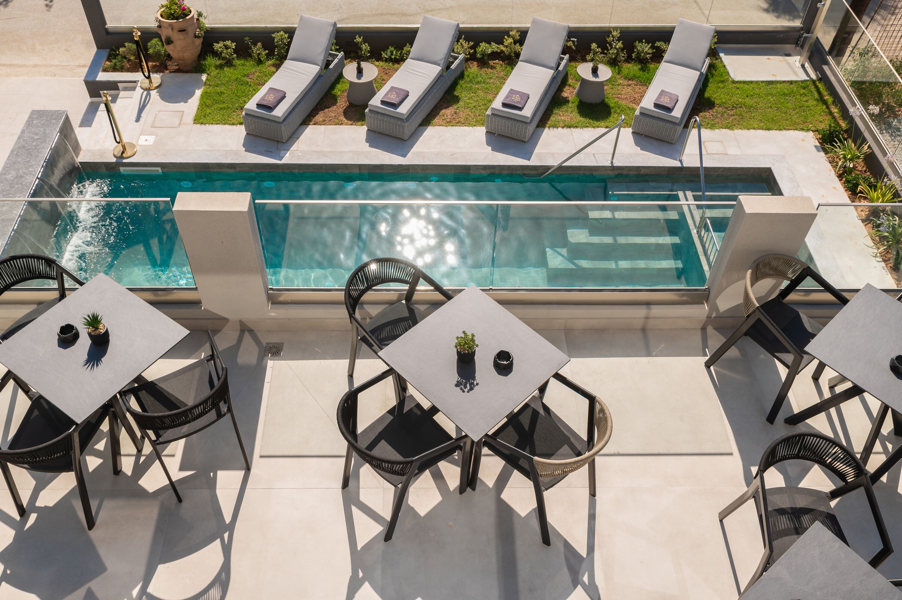 Zona de piscina en la azotea con sillones de descanso y mesas, rodeada por un muro bajo y plantas en macetas.