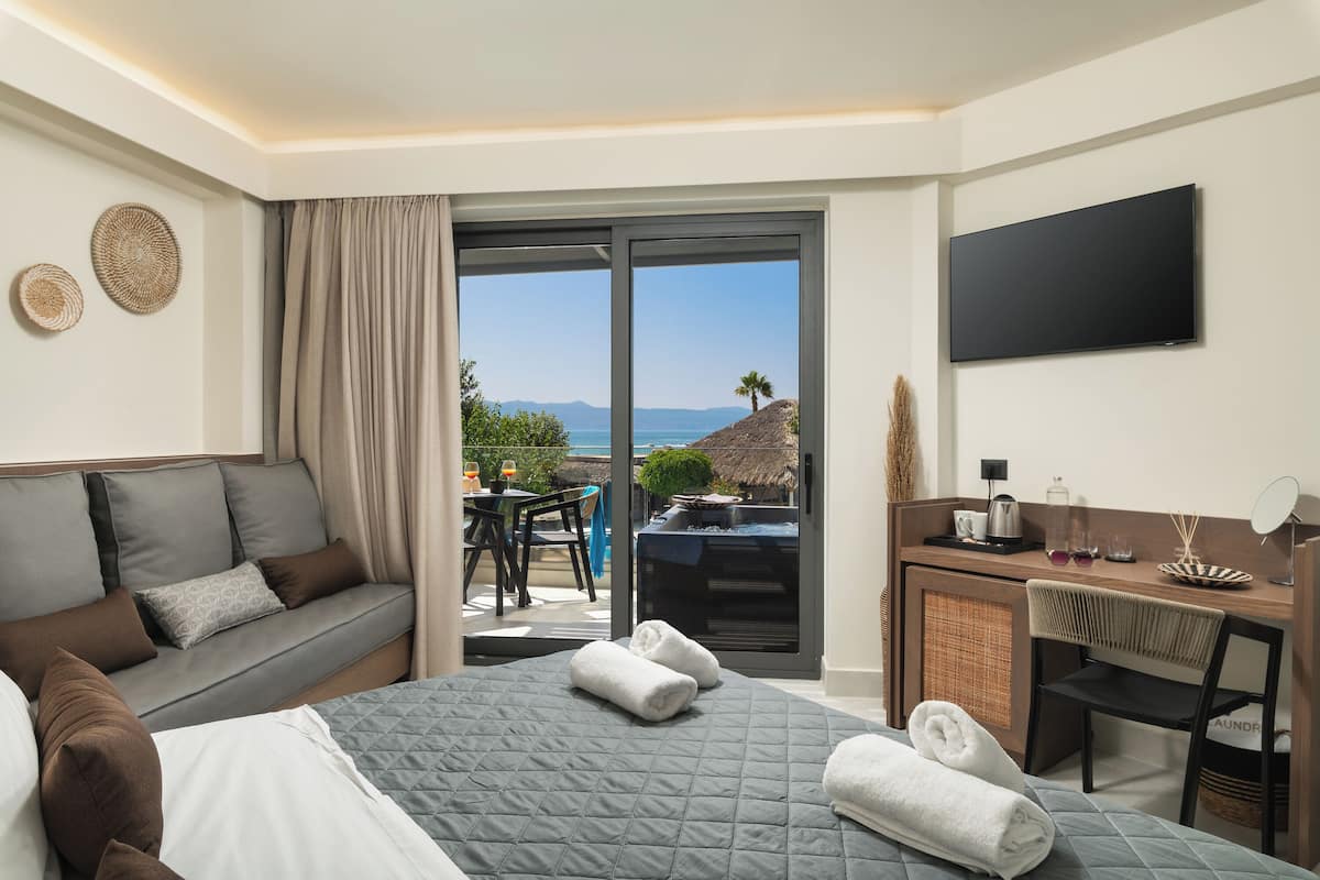 Une chambre d’hôtel avec un lit, un canapé, un bureau, une télévision et une vue sur la mer.