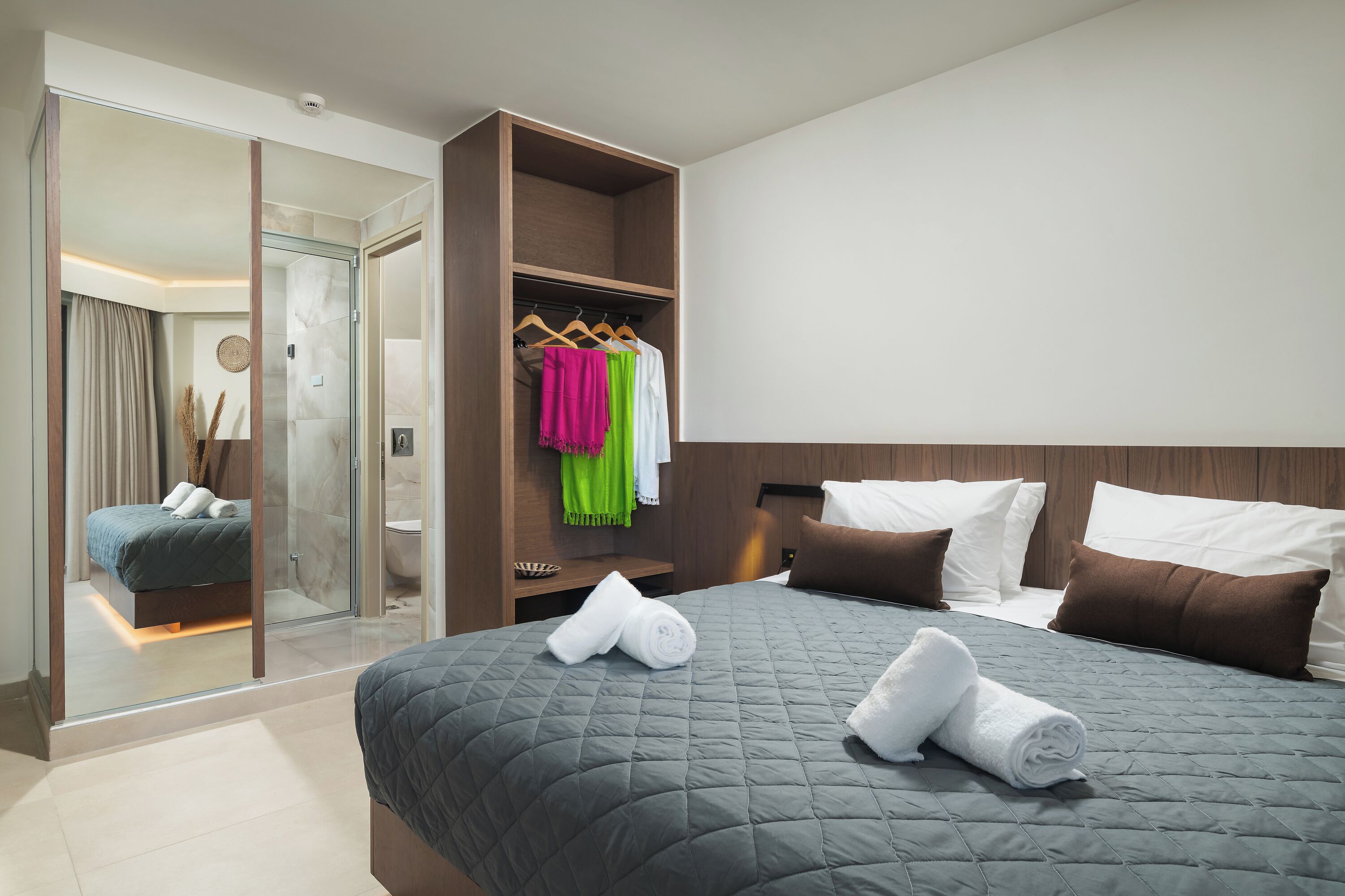 Une chambre d’hôtel moderne dotée d’un grand lit, d’un dressing et d’une salle de bain visible à travers une paroi en verre.