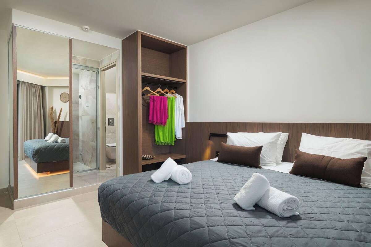 Une chambre d’hôtel moderne dotée d’un grand lit, d’un dressing et d’une salle de bain visible à travers une paroi en verre.