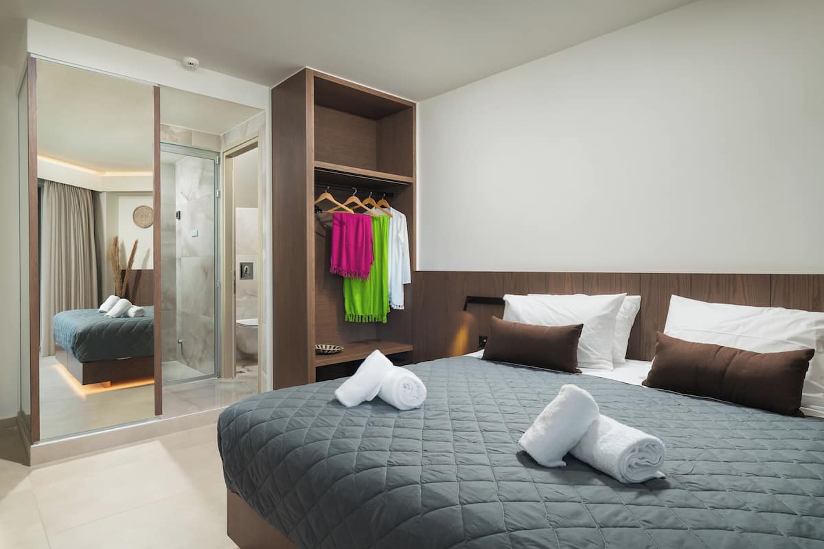 Ett modernt hotellrum med en stor säng, en rymlig klädkammare och ett badrum som syns genom en glasvägg.