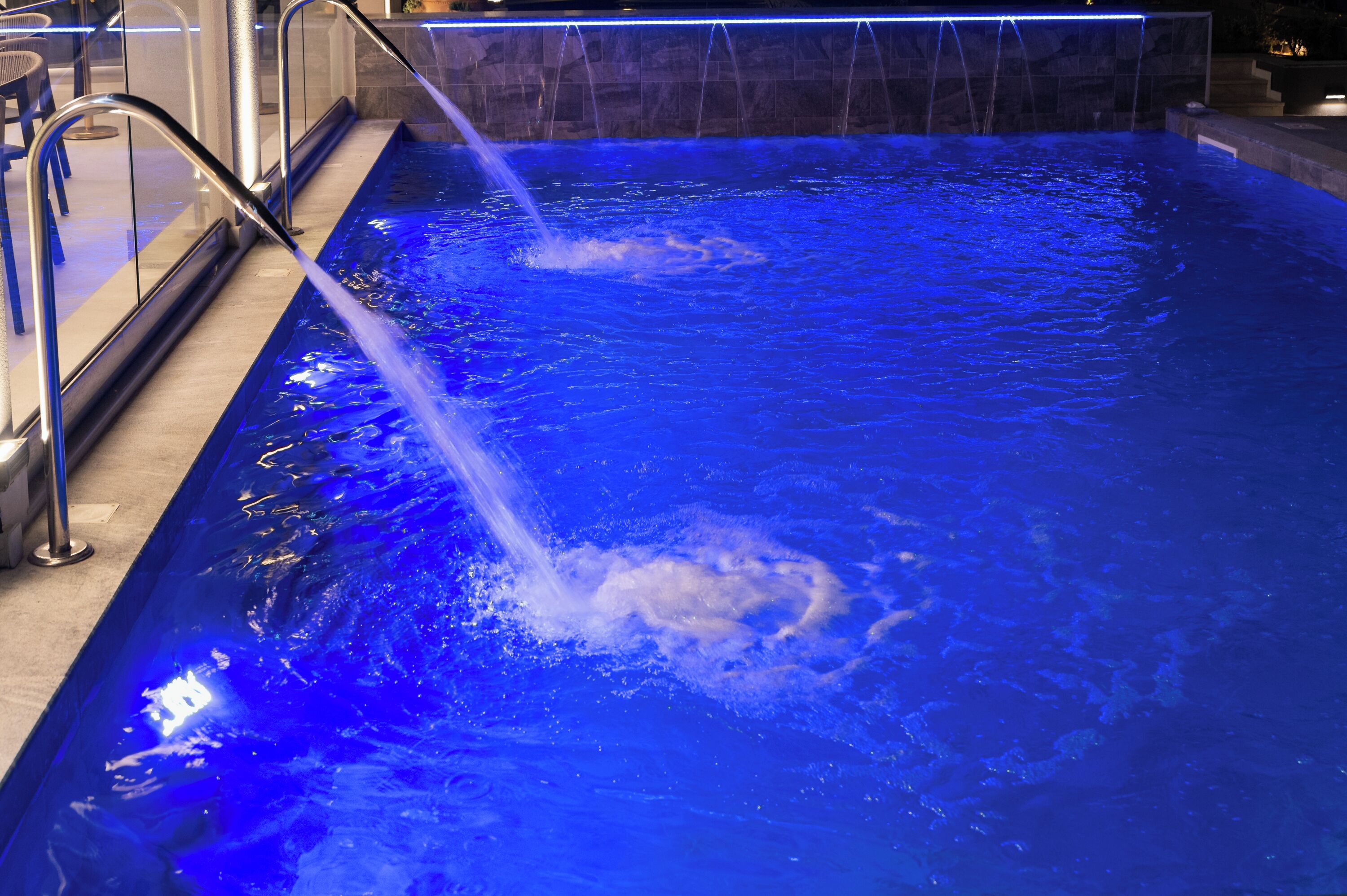 Une piscine aux eaux bleues, une fontaine et un mur de pierre en arrière-plan.
