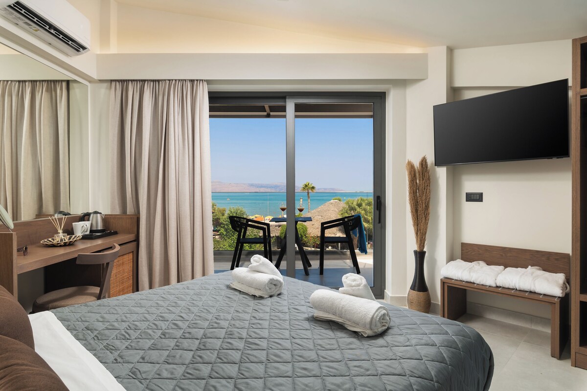 Habitación de hotel con cama, escritorio, silla, televisor y balcón con vista al mar.