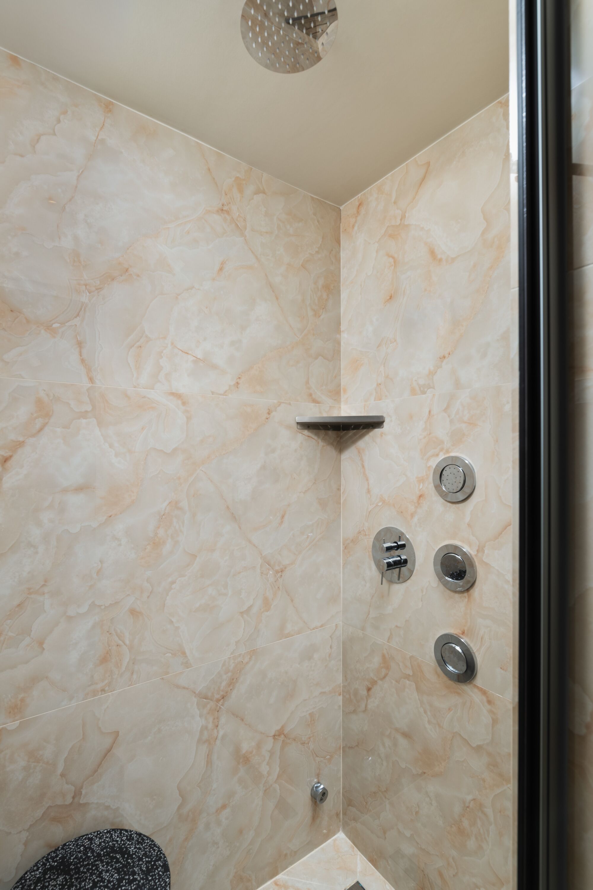 Un baño con paredes de mármol, ducha con cabezal de ducha manual y retrete.