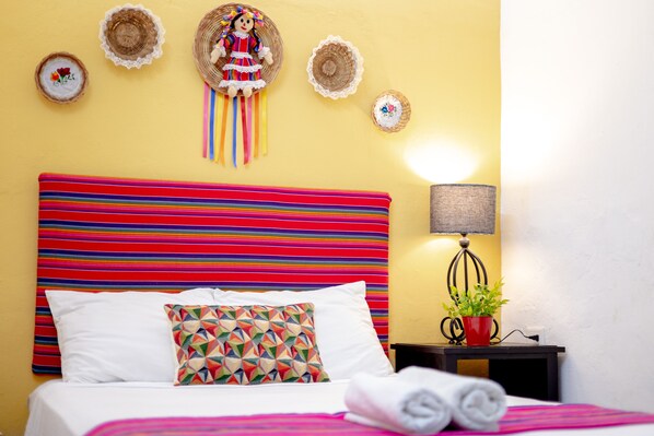 A hotel room with a colorful striped headboard, a decorative pillow, a wall-mounted hat, a bedside lamp, and a small potted plant. - Cozy house for 6 persons, near to san juan´s park with all services (Valladolid)