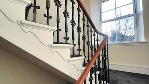 A staircase with ornate black railings and a wooden handrail, leading to a room with a large window.