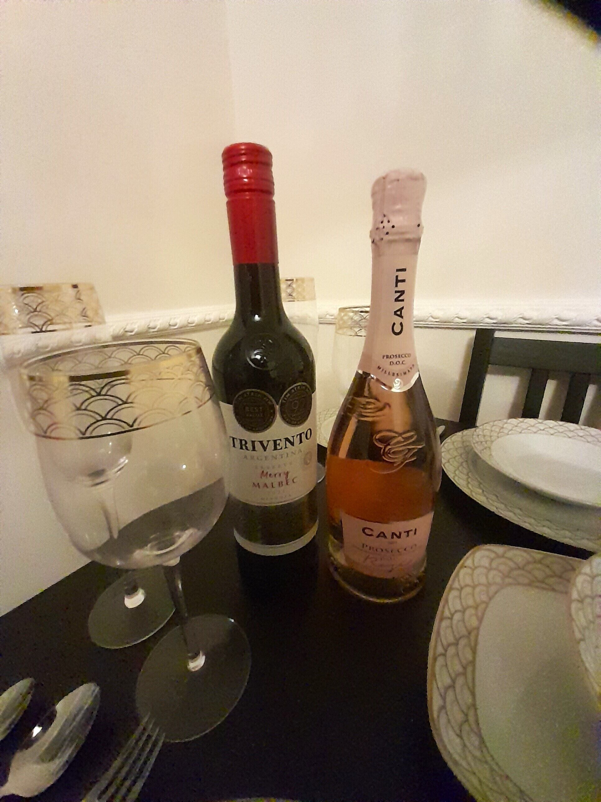 Une table avec deux bouteilles de vin, un verre et des couverts.