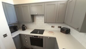 A compact kitchen with grey cabinets, a microwave, a coffee maker, a toaster, and a dishwasher.