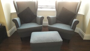 Two armchairs with matching cushions and a matching ottoman in a room with wooden flooring and a window with blinds.