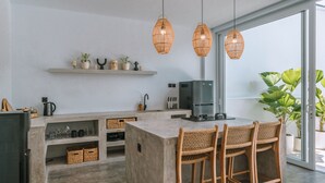 A modern kitchen with a central island, wicker chairs, and pendant lights. - Villa Seseh Breeze (Cemagi)