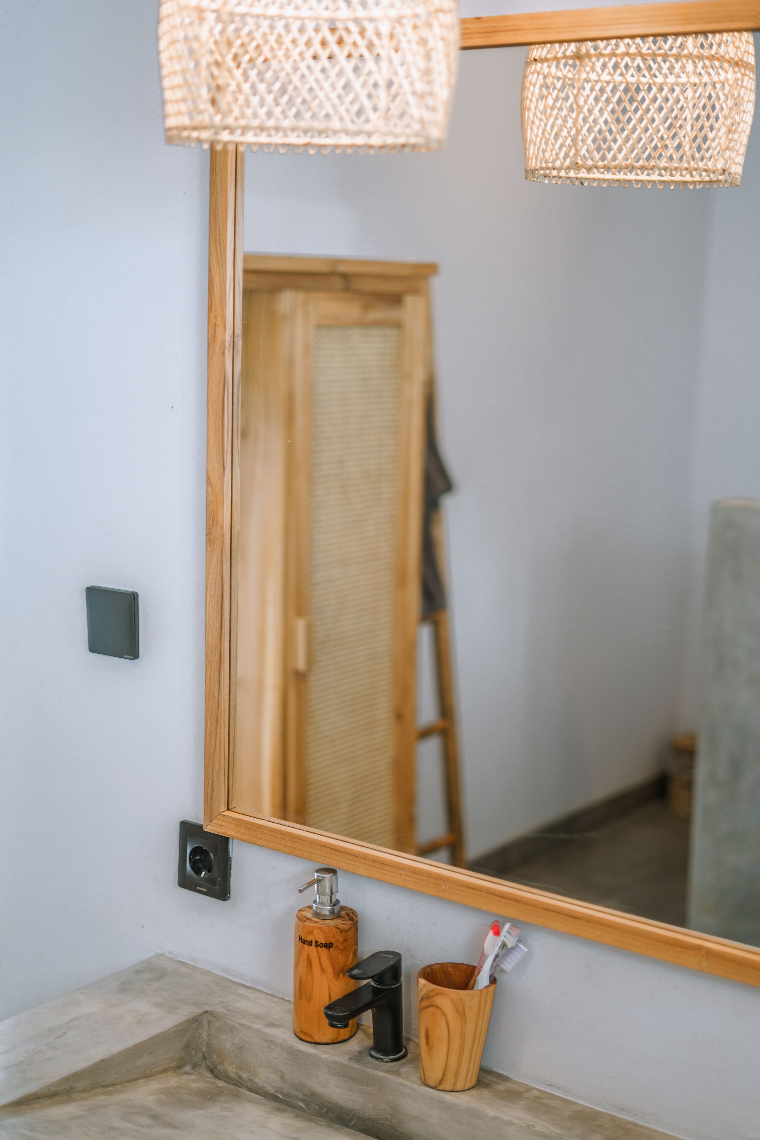 Un baño con un espejo de marco de madera, un dispensador de jabón y una taza de madera con cepillos de dientes.