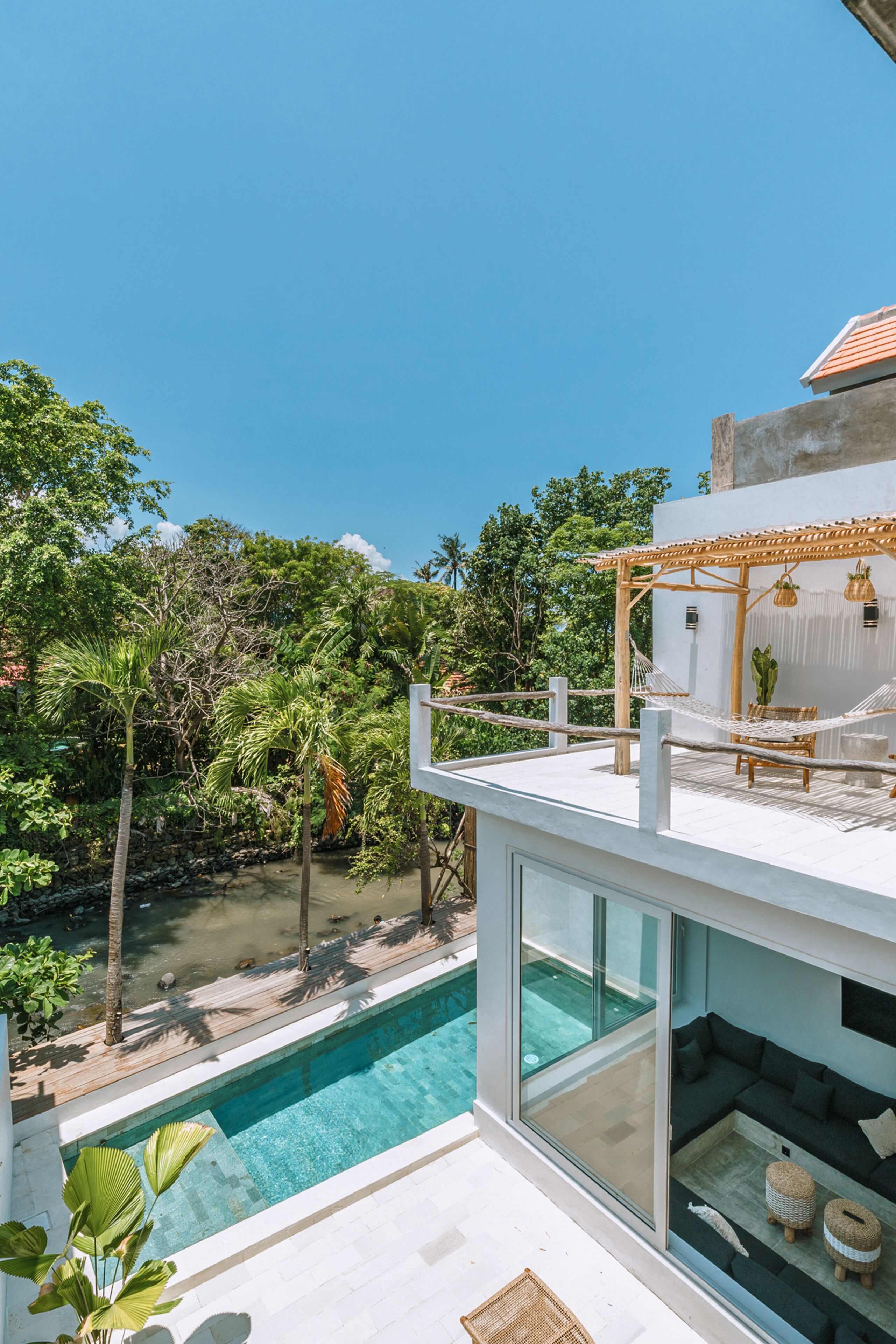 A modern house with a glass pool, a hammock, and a view of lush greenery.