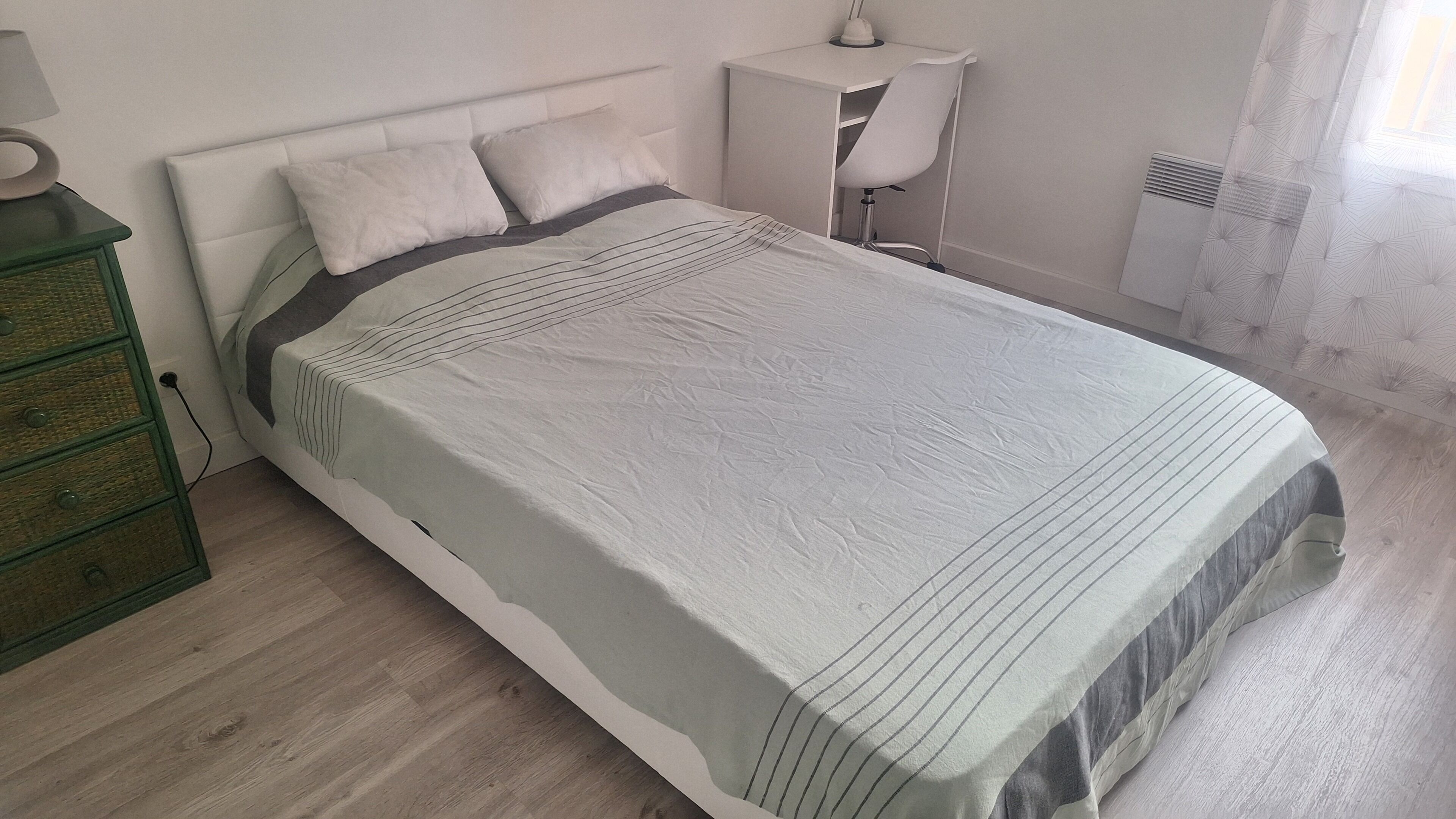 A neatly made bed with a striped bedspread, a bedside table with a lamp, and a dresser with drawers.