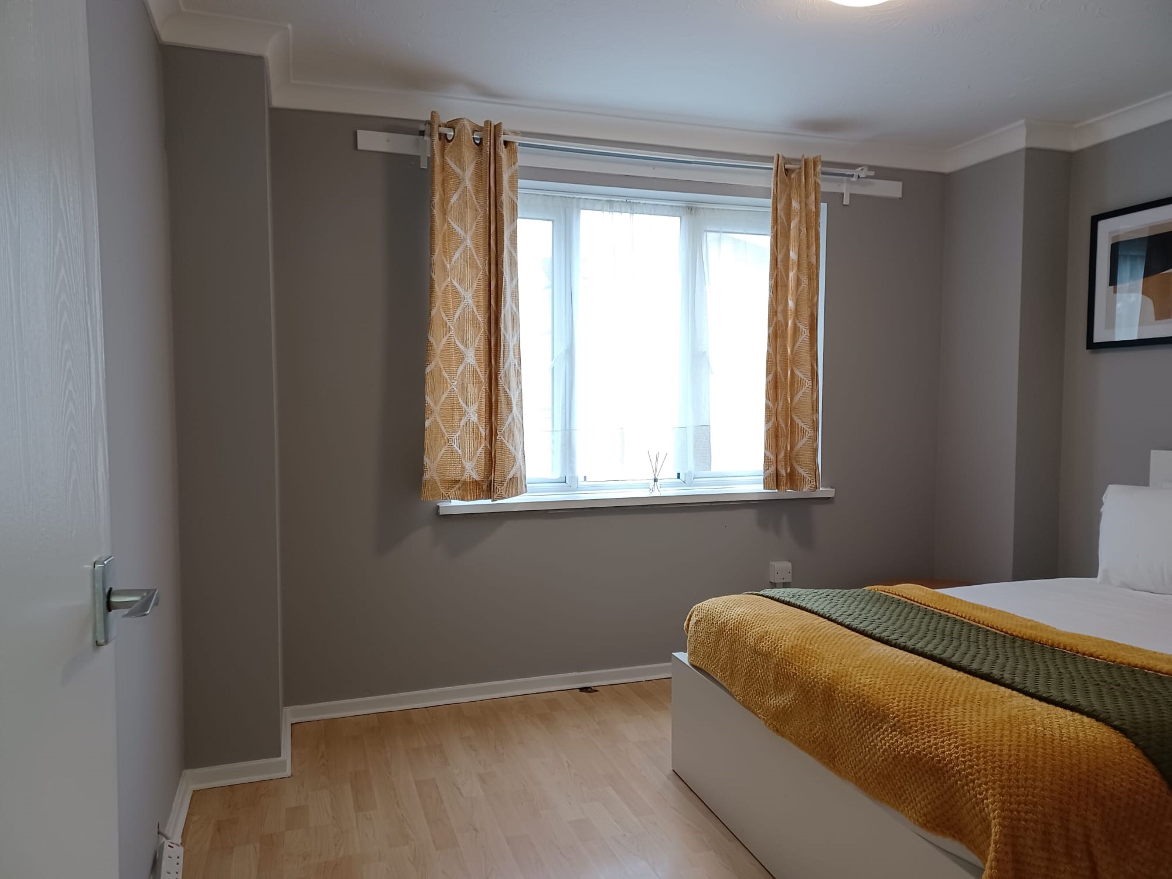 A bedroom with a bed, a window with patterned curtains, and a white wall.