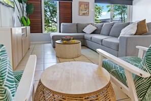 Relax in this stylish living room with a grey sofa, round coffee table, and armchair, offering a view of lush greenery.