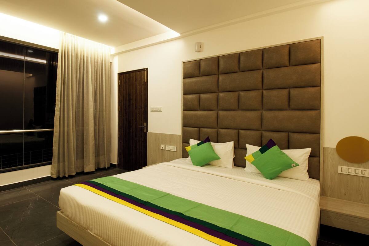 Habitación de hotel con una cama grande, una ventana con cortinas, un cabecero de madera y una lámpara fijada a la pared.