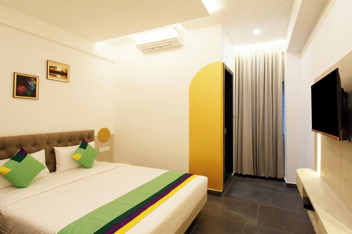 Habitación de hotel con cama, televisor de pantalla plana montado en la pared y baño con cortina de ducha.