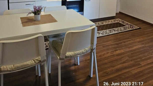Une cuisine moderne avec des meubles blancs, une hotte en acier inoxydable et un four encastré. On y trouve une table à manger avec des chaises et une petite plante posée sur la table.