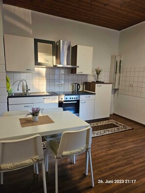 Une cuisine moderne avec des meubles blancs, une hotte en acier inoxydable et un four encastré. On y trouve une table à manger avec des chaises et une petite plante posée sur la table.