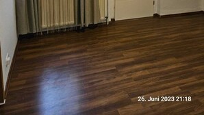 Une pièce avec un plancher en bois, une porte blanche et une fenêtre avec des rideaux.