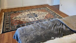 Une pièce dotée d’un téléviseur à écran plat fixé au mur, d’un tapis à motifs sur le plancher en bois et d’une porte donnant sur une autre pièce.