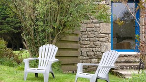 Deux chaises Adirondack blanches, placées dans un espace verdoyant, avec un mur de pierres et une clôture en bois.