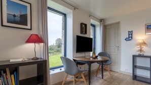 Une pièce comprenant un bureau, deux chaises, un téléviseur, une bibliothèque et une fenêtre donnant sur un beau paysage.