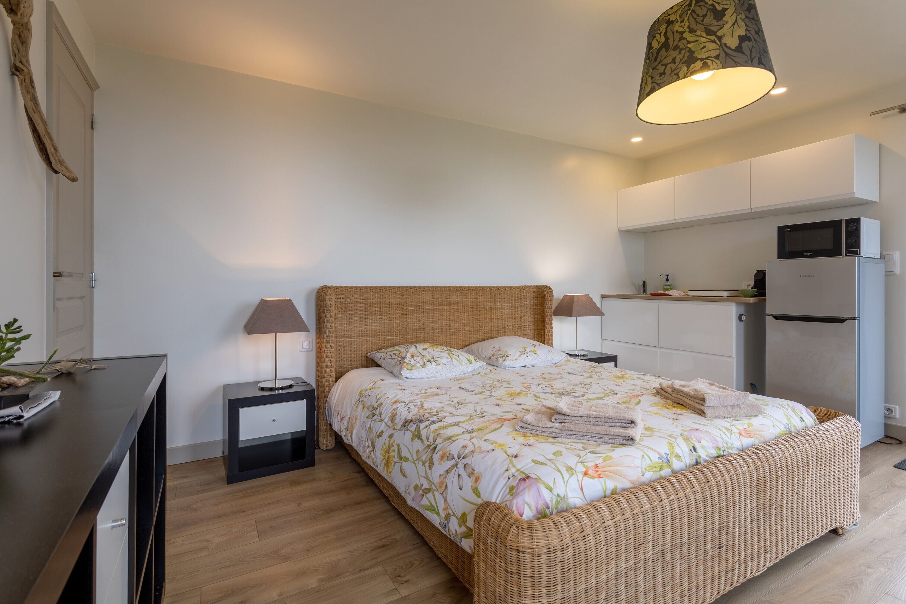 Ein Schlafzimmer mit Bett, Nachttischen, einer Lampe, einem Schreibtisch und einer Küchenzeile.