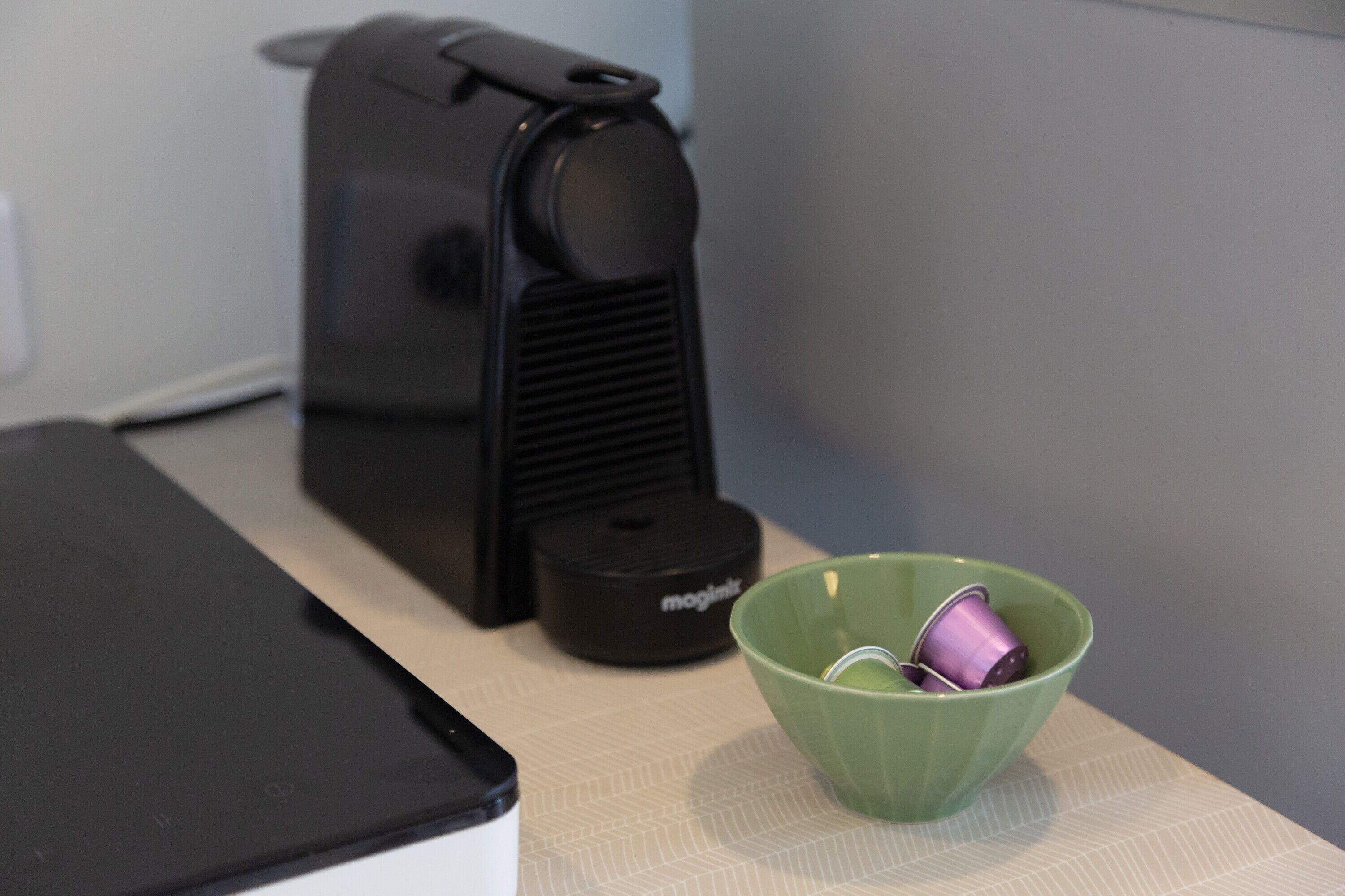 Une machine à café, un bol vert contenant un objet violet et un appareil noir posés sur une table.