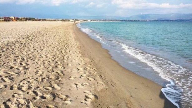 Una playa con huellas, cielo despejado y edificios a lo lejos.