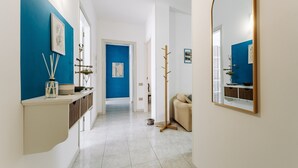 Un pasillo con una pared azul decorativa, un espejo, un perchero y una puerta que da a otra habitación.
