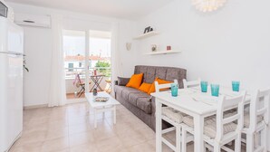 Un appartamento moderno con zona pranzo, un divano con cuscini arancioni, un tavolo bianco e un balcone con vista.