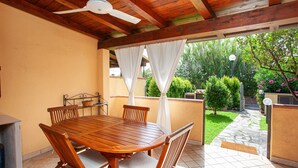 Una mesa y sillas de madera bajo un ventilador de techo, con vista a un jardín a través de una puerta abierta.