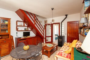 A living room with a staircase, a dining table, a sofa, and a television.