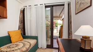 Una habitación con un sofá verde, una mesa con lámpara y un ventanal corredizo que da a un espacio exterior.
