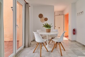 A dining area with a round table, white chairs, a potted plant, and wall decor.