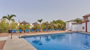 Ein Pool mit Liegestühlen, Palmen und einem Gebäude mit einem Ziegeldach.