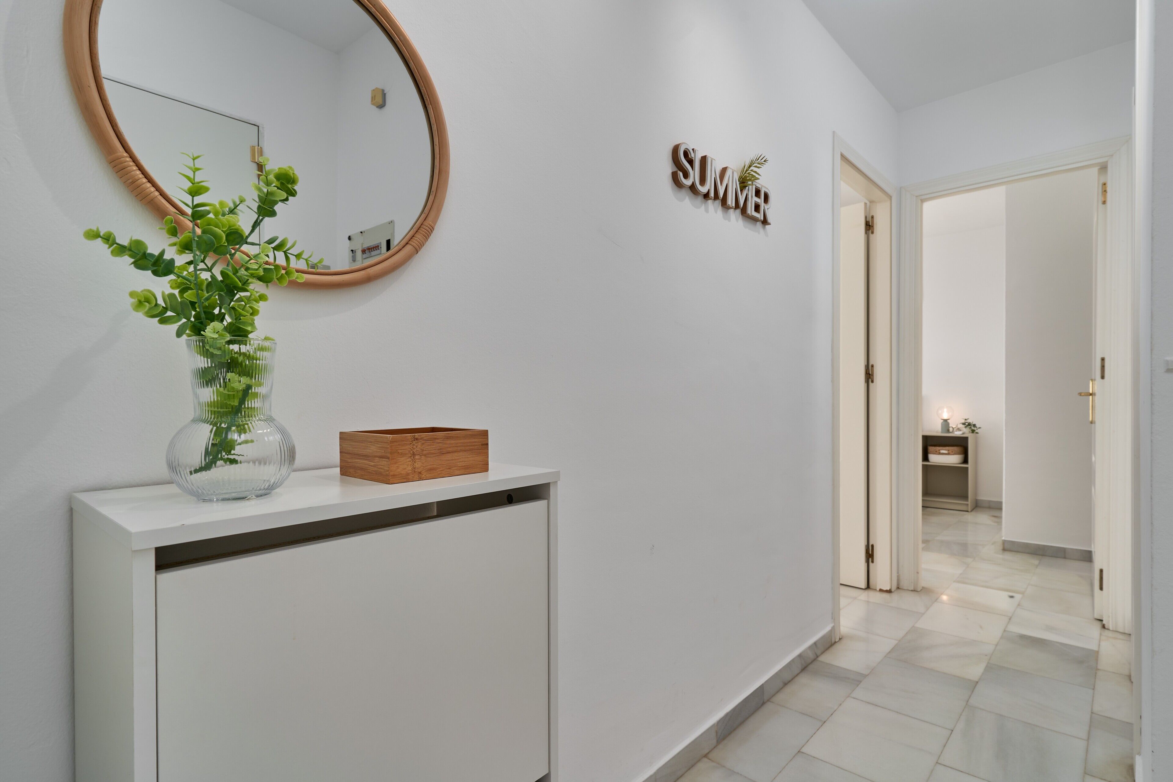 A hallway with a white console, a round mirror, a wooden sign, and a plant.