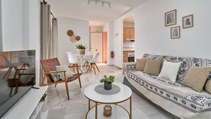 Ein modernes Wohnzimmer mit Sofa, Fernseher, Couchtisch und einem Essbereich mit Stühlen und Tisch.