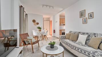 A modern living room with a sofa, TV, coffee table, and a dining area with chairs and a table.