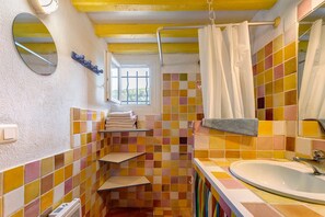 Une salle de bain avec un sol carrelé, un lavabo, un miroir, une fenêtre et un rideau de douche.