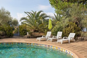 Une piscine à l’eau claire, entourée de chaises longues et d’un parasol vert.