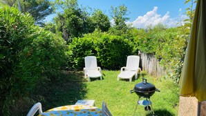 En terrasse med et bord og stole, grill og en frodig have.