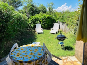 Un patio con tavolo e sedie, un barbecue e un giardino rigoglioso.