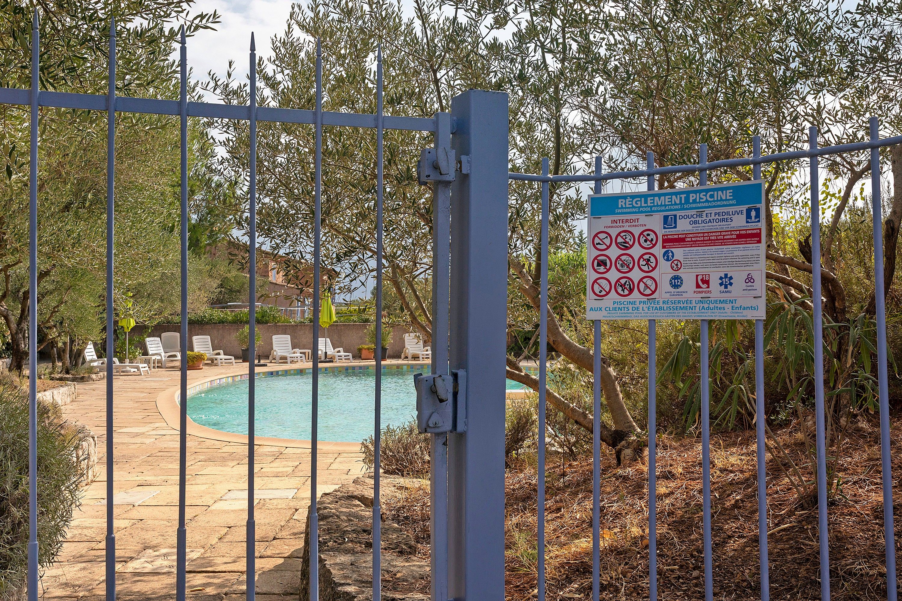 Une piscine entourée d’une clôture, avec un panneau indiquant les règles d’utilisation de la piscine.