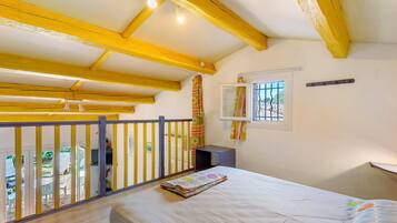 A room with a bed, a window with bars, a small table, and a balcony with yellow railings.