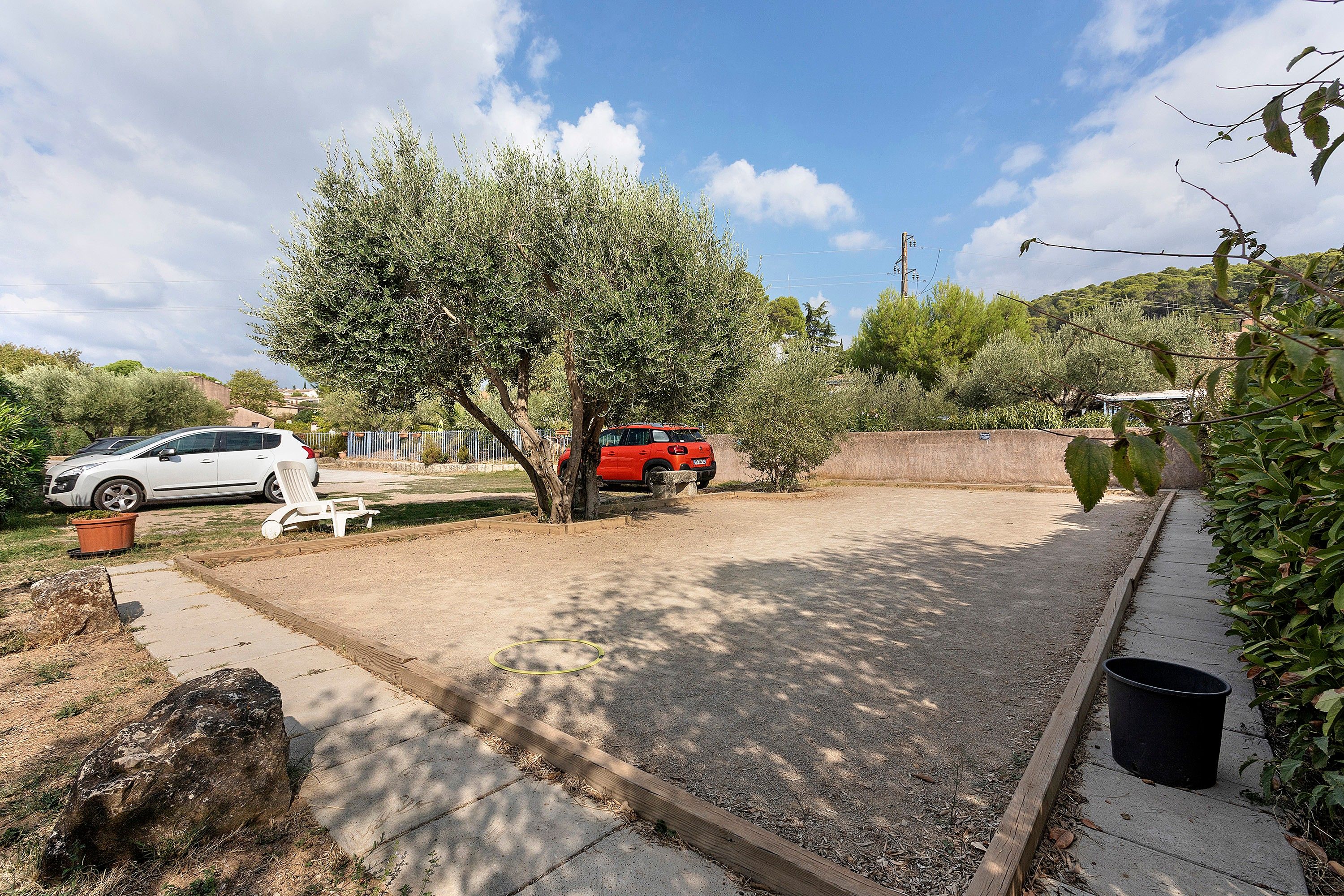 A parking area with two cars, a tree, and a garden bed.