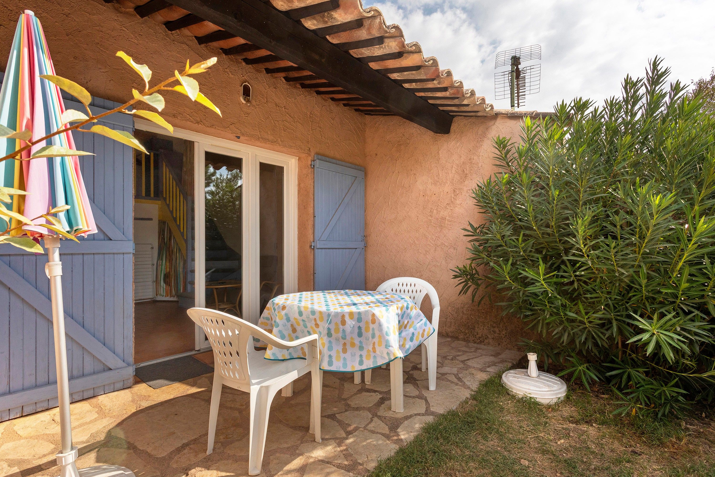 Une terrasse extérieure avec une table et des chaises, un parasol coloré et un mur en pierre.