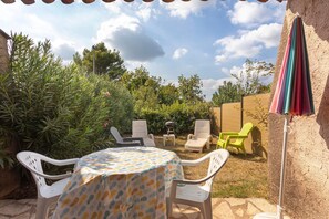 Une terrasse extérieure avec une table ronde, des chaises blanches et un parasol coloré.